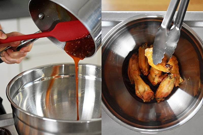 A saucepan is pouring sauce into a metal mixing bowl and adding crispy chicken wings in the bowl.