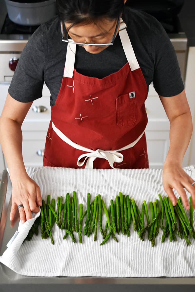 Someone in a red apron has cooked asparagus on a large white kitchen towel.