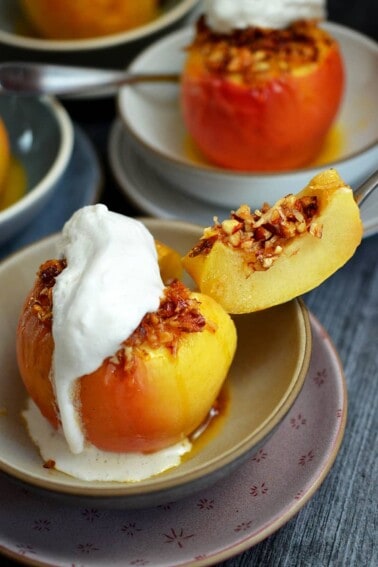 A baked apple topped with whipped coconut cream has a slice cut out of it to show the inside.
