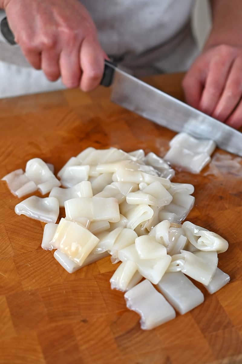 Slicing cleaned calamari into 3/4-inch rings on a wooden cutting board.
