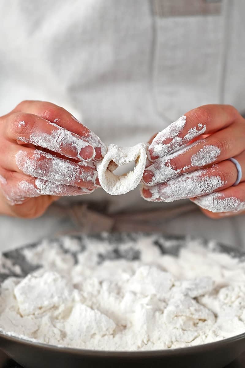 Two hands are dredging a calamari ring in a shallow dish filled with grain-free flour.