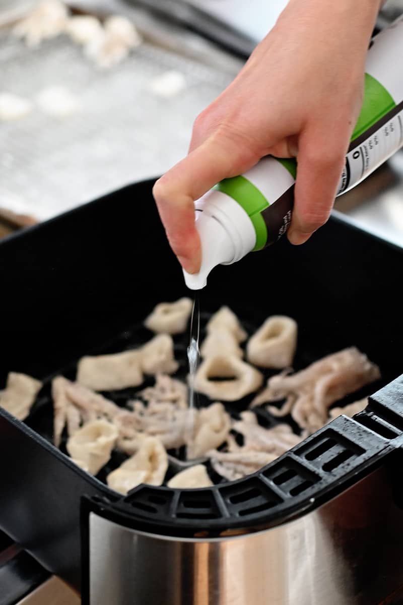 Spraying avocado oil on calamari in an air fryer basket