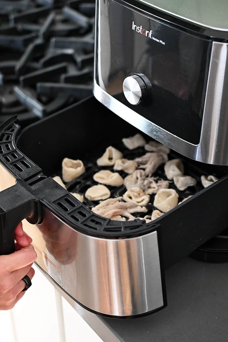 A hand is closing an air fryer filled with calamari.