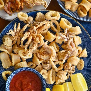 An overhead shot of three plates with paleo and gluten-free fried calamari. There is a small bowl with marinara sauce in it and lemon wedges on the side