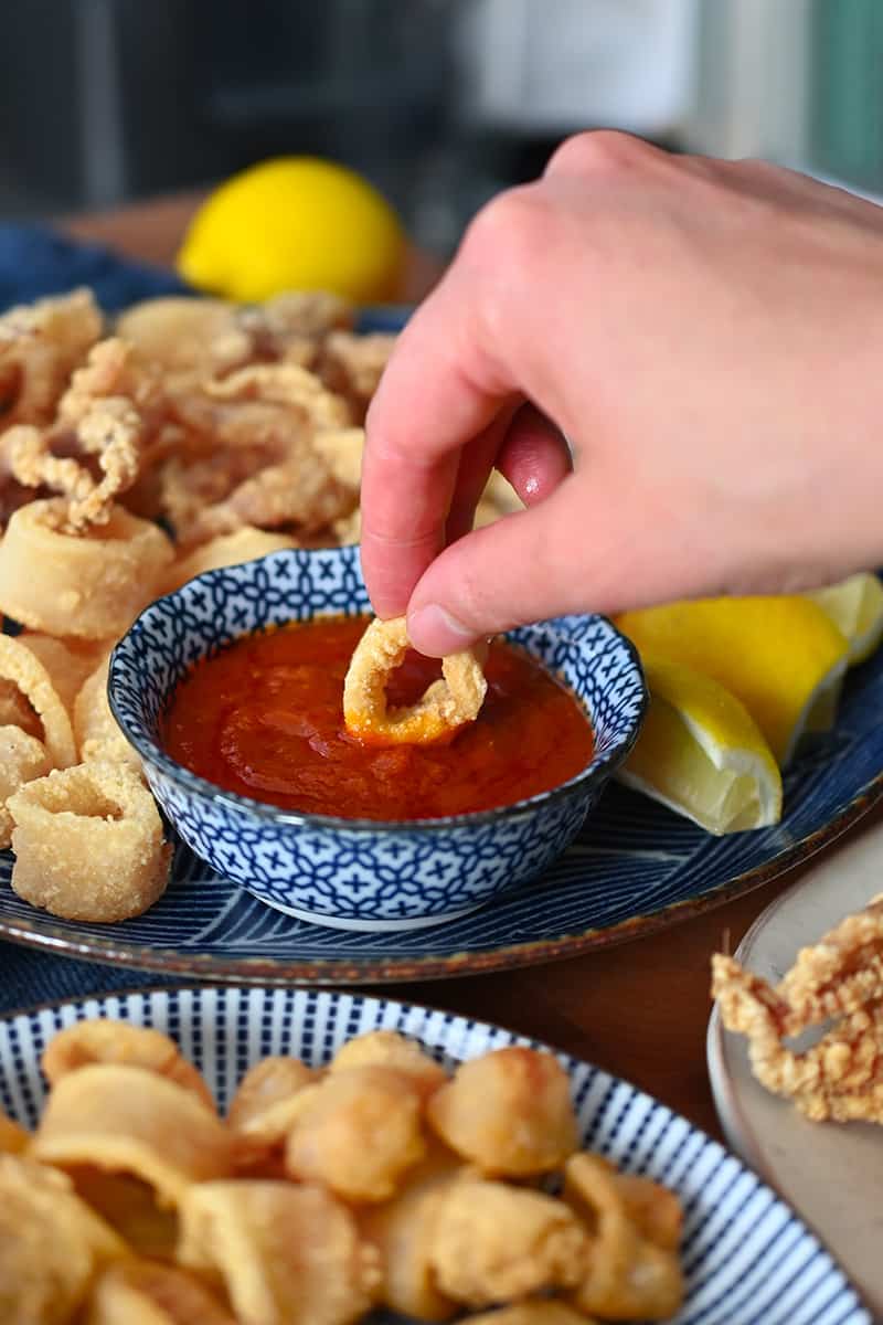 A hand dipping paleo and gluten-free fried calamari in a bowl of marinara sauce.