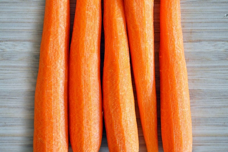 An overhead shot of five peeled carrots on a wooden cutting board.