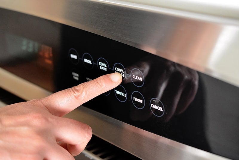 A finger pressing the convection roast button on an oven display.