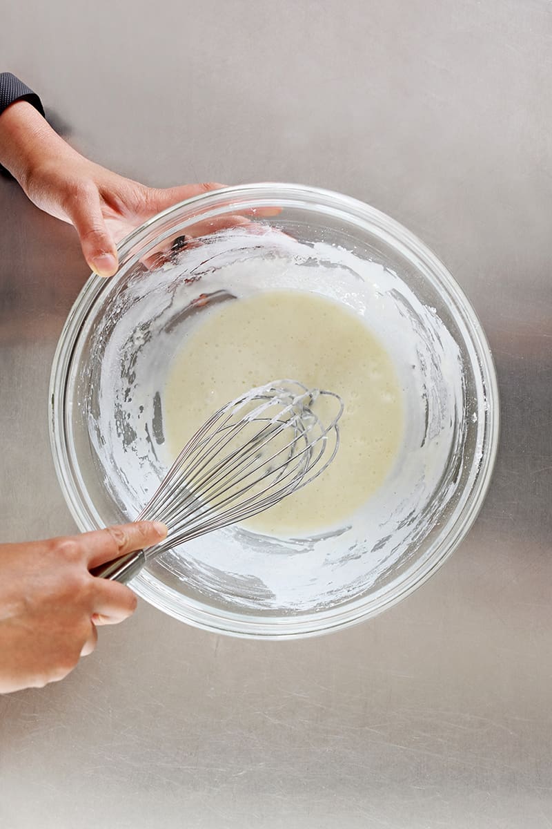 An overhead shot of someone whisking the batter for Nom Nom Paleo's Baked Buffalo Cauliflower 