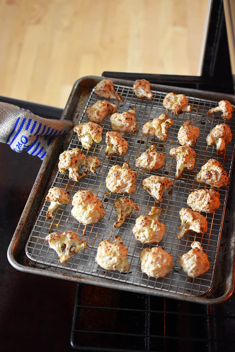 A gloved hand is removing a tray of golden brown Baked Buffalo Cauliflower from the oven.