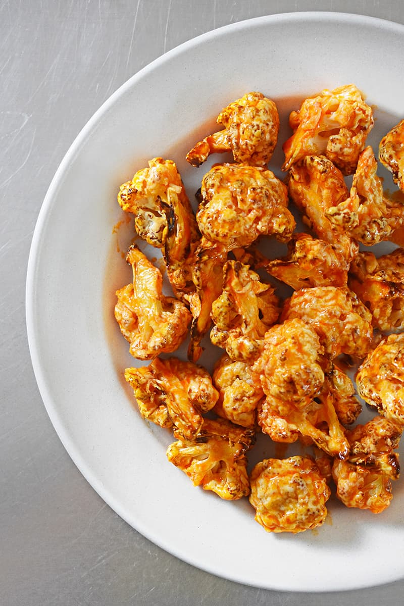 Overhead shot of baked buffalo cauliflower in a white round platter.