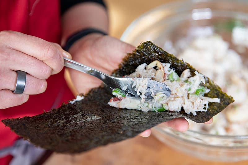 Someone adding the filling to the California hand roll on a rectangular piece of toasted nori.