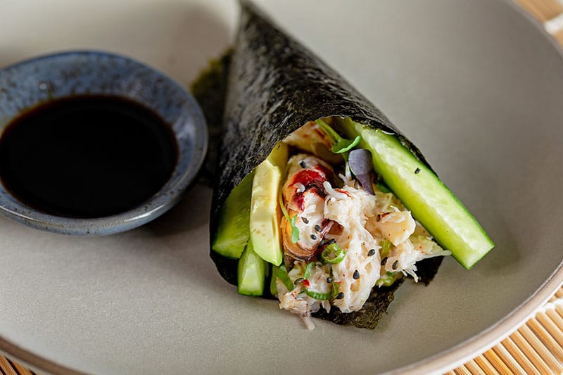 Closeup up of a homemade California hand roll filled with crab, avocado, and cucumbers.