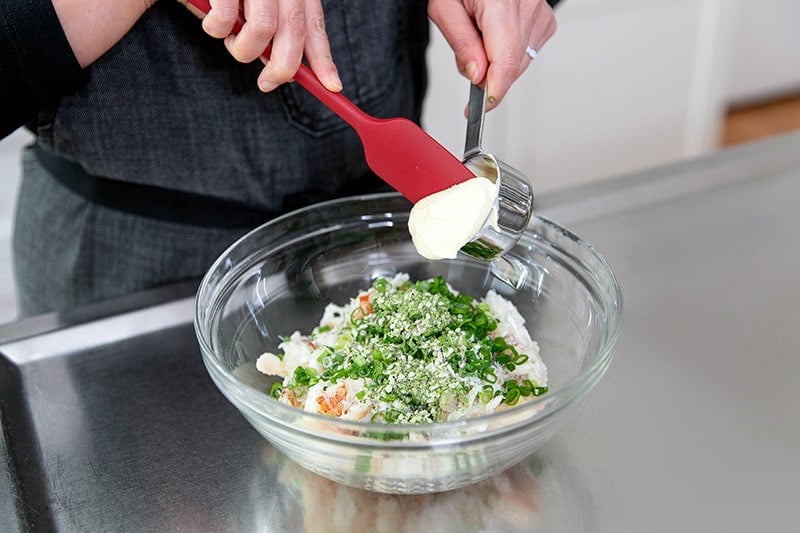 A large glass bowl filled with crab, scallions, coconut flour, seafood seasoning, and mayonnaise.