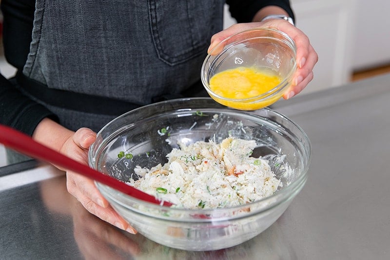 Pouring a whisked egg into the crab cake mixture.