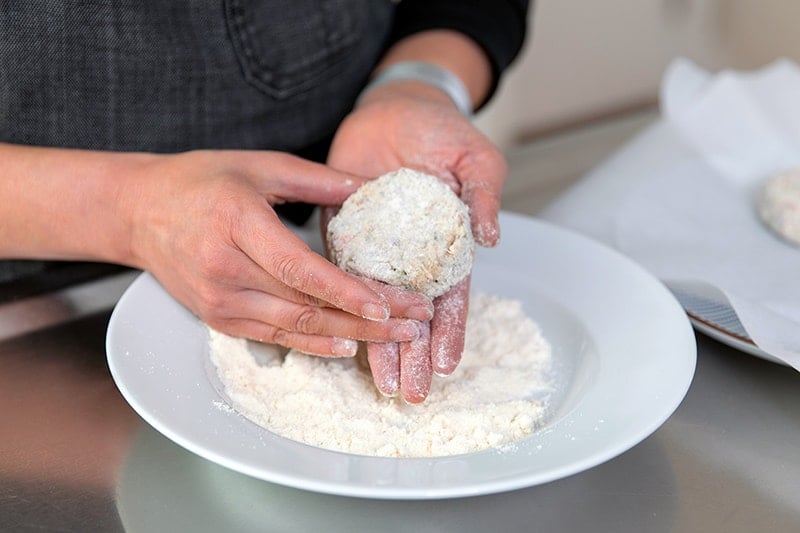Someone coating a paleo crab cake with coconut flour.