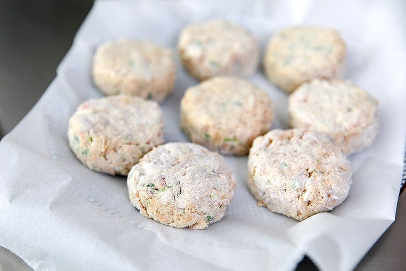 A parchment paper lined plate is filled with paleo crab cakes that are waiting to be fried.