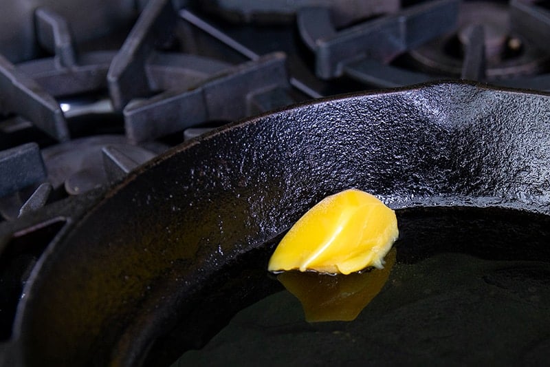 Ghee is melting in a cast iron skillet to fry paleo and keto crab cakes.