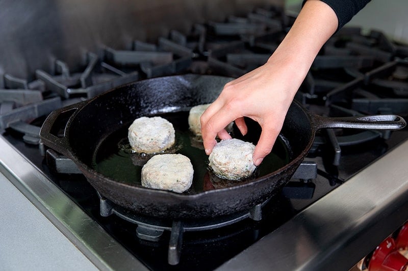 Adding paleo crab cakes to a cast iron frying pan.