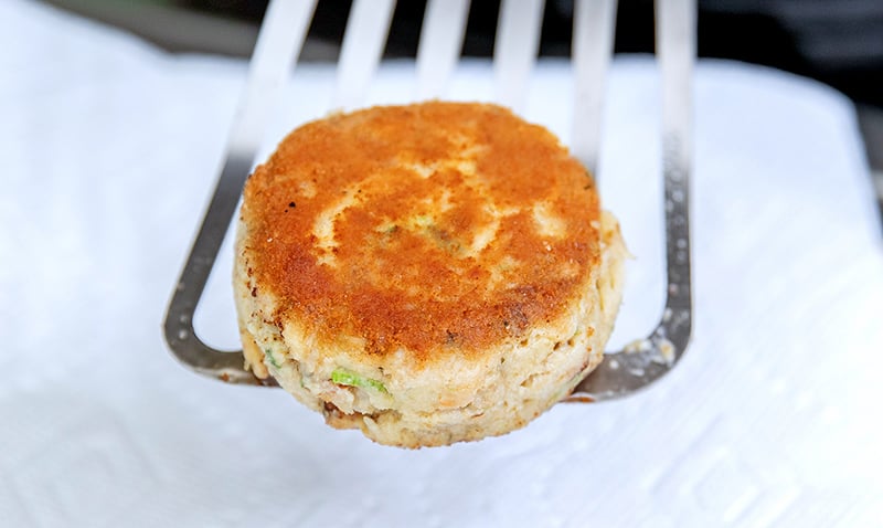 A closeup shot of a golden brown paleo and keto crab cake on a fish spatula. 