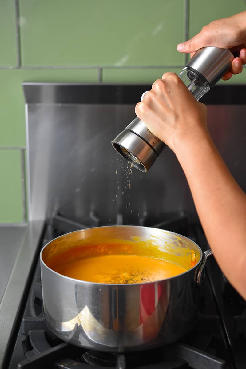 Someone cracking black pepper into a saucepan filled with cream of tomato soup