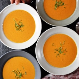 An overhead shot of four bowls filled with Whole30-friendly, paleo, and dairy-free Cream of Tomato Soup topped with basil