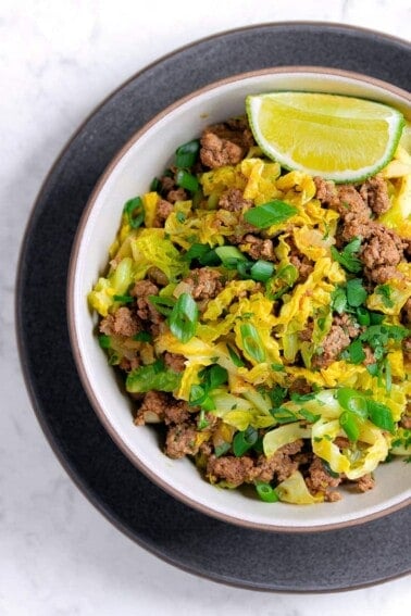 An overhead shot of an Indian-inspired beef and cabbage stir-fry with a lime wedge on the side.