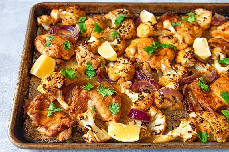 An overhead view of sheet pan Tandoori Chicken fresh from the oven with lemons and cilantro on top.