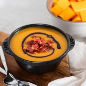 A black bowl filled with Instant Pot Butternut Squash Soup on a wooden cutting board.