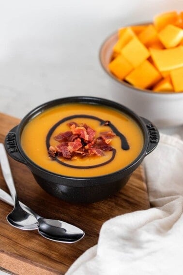 A black bowl filled with Instant Pot Butternut Squash Soup on a wooden cutting board.