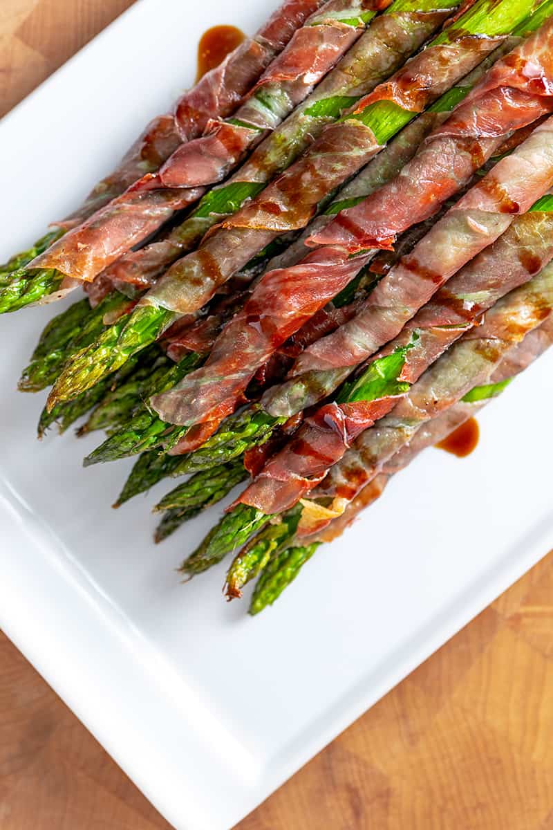 An overhead shot of prosciutto-wrapped asparagus on a white plate.
