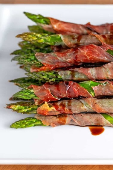A closeup shot of broiled prosciutto-wrapped asparagus topped with aged balsamic vinegar.