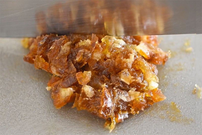 A closeup of a chef's knife mincing Medjool dates on a gray cutting board.