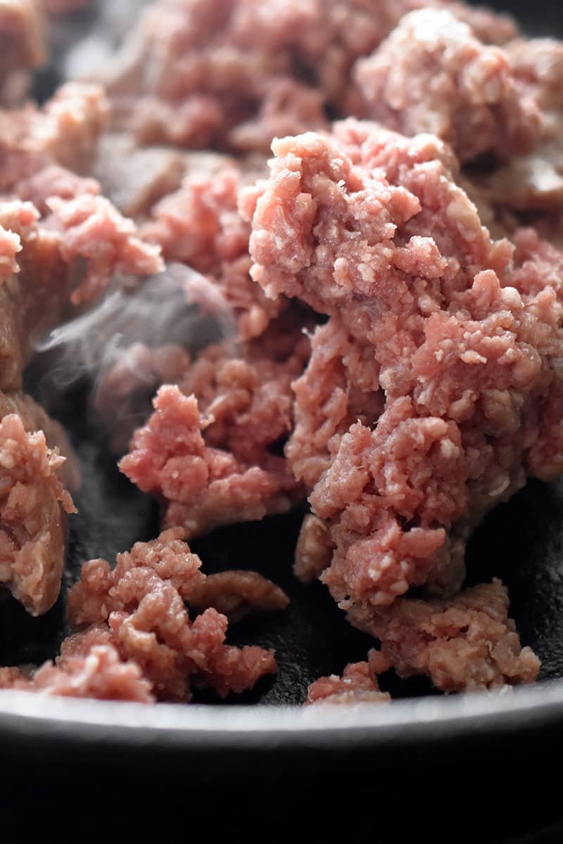 Close up shot of raw ground beef in a skillet to make Tex-Mex Beef and Cauliflower Rice Casserole.
