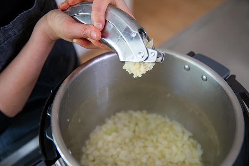 Adding minced garlic to an open Instant Pot filled with sauteed onions to make Whole30 Atakilt Wat, Ethiopian Cabbage Stew.