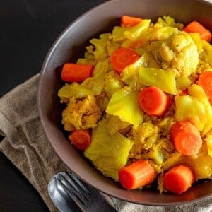 An overhead shot of a brown bowl filed with Atakilt Wat, Ethiopian cabbage stew.