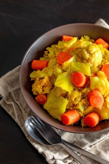 An overhead shot of a brown bowl filed with Atakilt Wat, Ethiopian cabbage stew.
