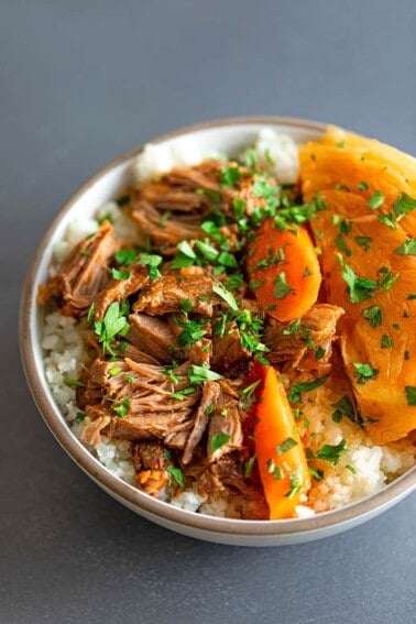 An overhead shot of a white bowl filled with Instant Pot Cheater Pork and Cabbage Stew over some cauliflower rice.