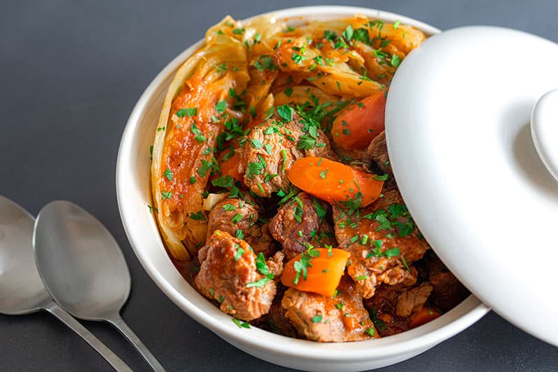 A side view of a partially covered white bowl filled with Whole30 Instant Pot Cheater Pork Stew, a pork and cabbage dish