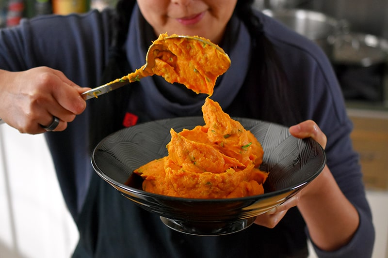Scooping up Instant Pot Mashed Sweet Potatoes into a black bowl.