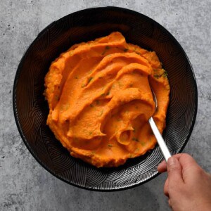 An overhead shot of a a hand scooping vegan and paleo Instant Pot Mashed Sweet Potatoes from a black bowl.