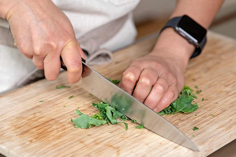 Slicing kale leaves into thin strips with a chef's knife on a wooden cutting board.