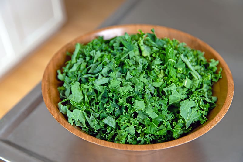 A large wooden bowl filled with sliced kale for a simple winter salad.