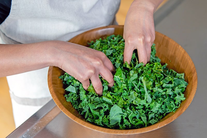 Two clean hands massaging the kale with the lemon vinaigrette.