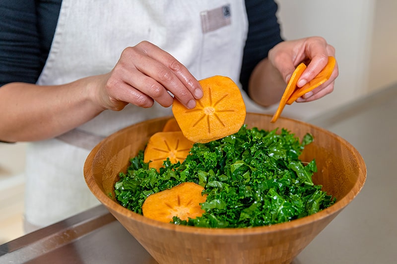 Adding thin slices of fuyu persimmons to a healthy kale salad dressed with a lemon vinaigrette