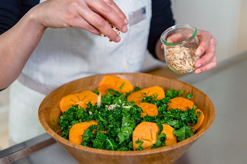 Sprinkling toasted almond slices on top of a kale salad with persimmons.