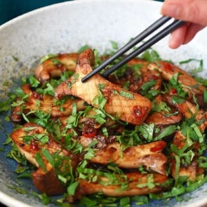 A pair of black chopsticks is picking up a piece of King trumpet mushrooms with Thai Chili peppers and lime from a light blue bowl.
