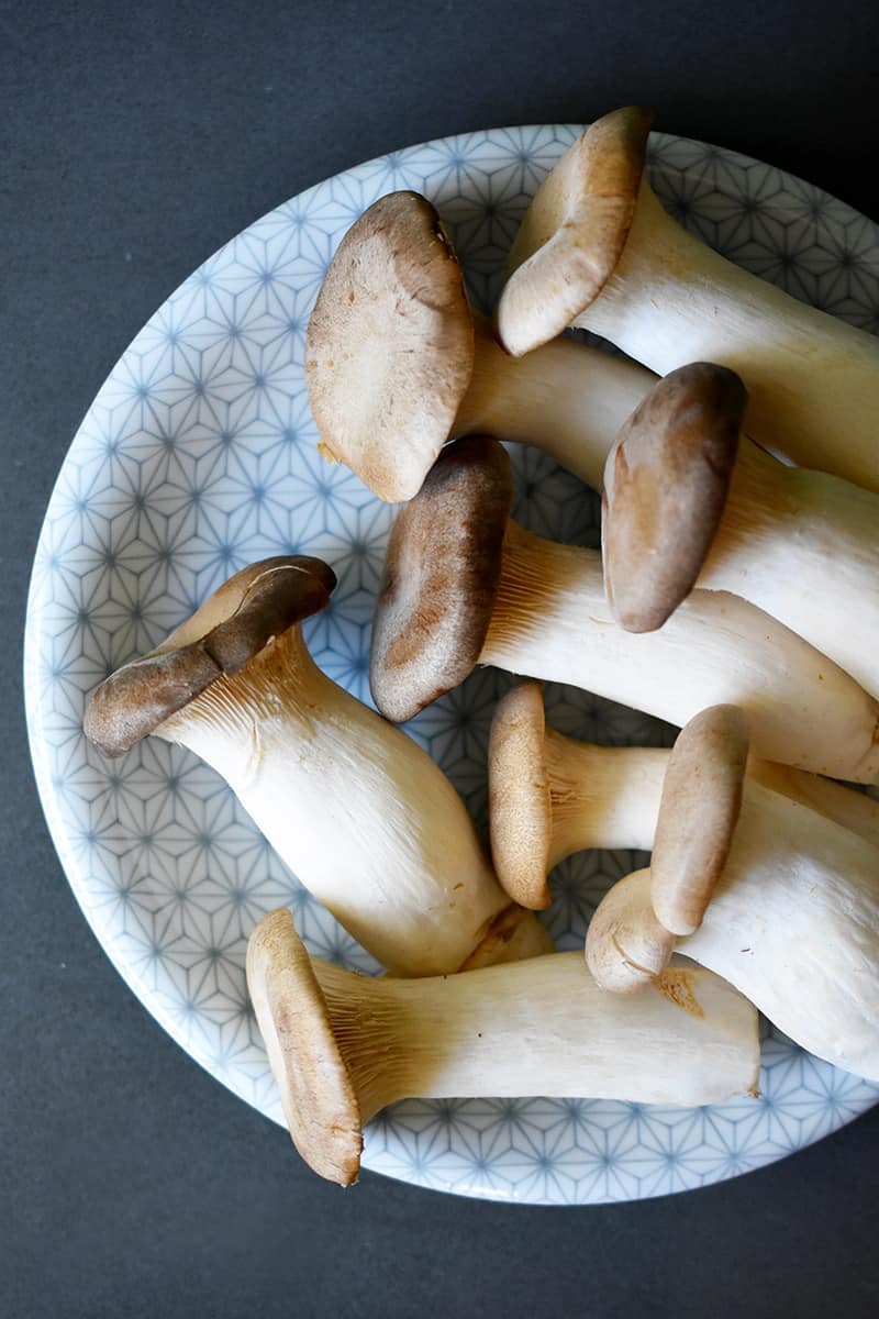 An overhead shot of a gray and white patterned plate filled with raw king oyster mushrooms.