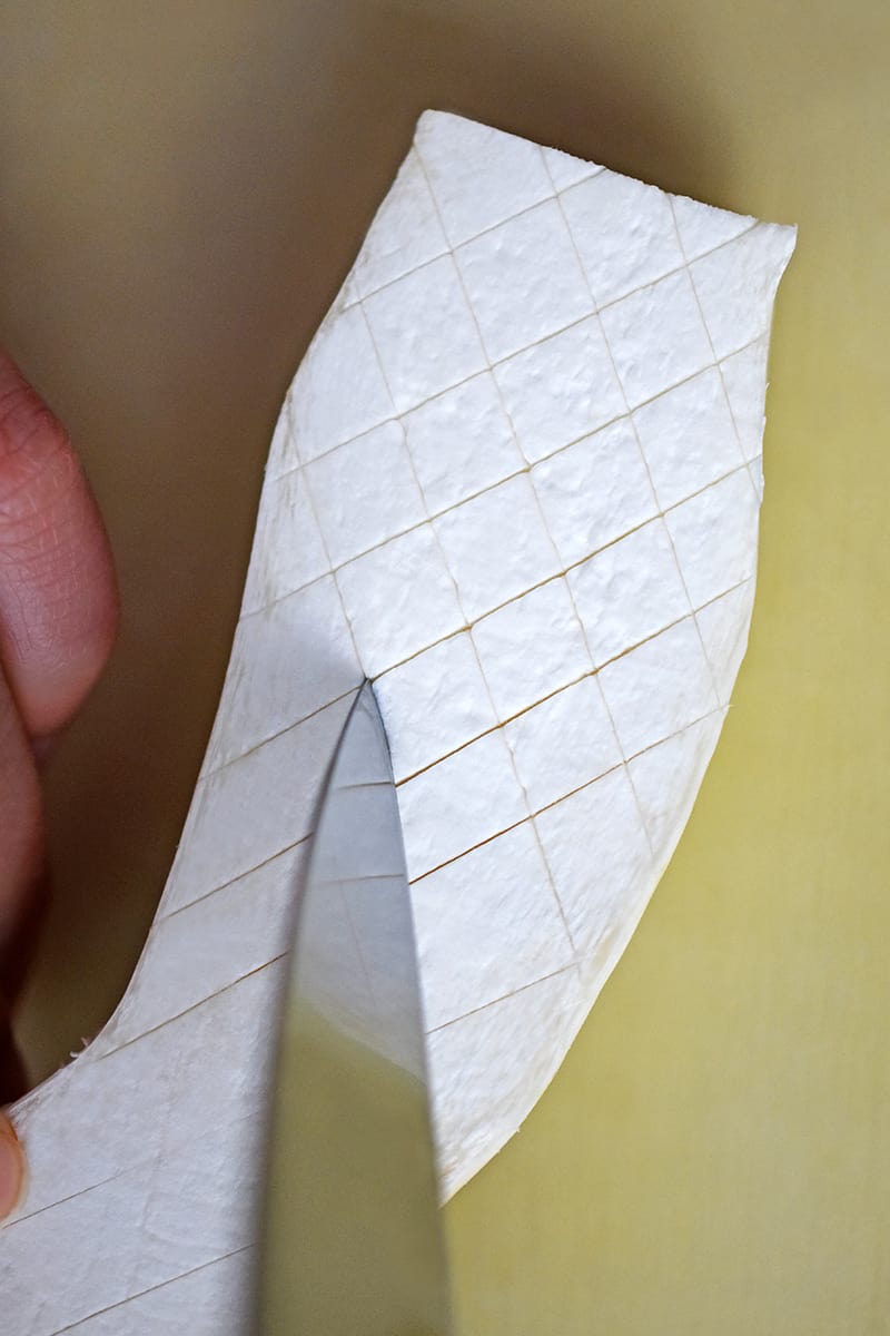 A sharp paring knife is cutting a shallow criss-cross pattern on the cut side of the king oyster mushroom