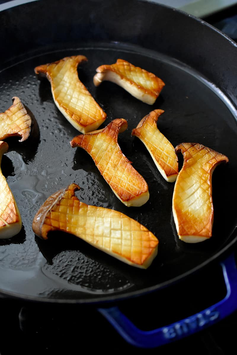 Overhead shot of browned king oyster mushrooms outside up in a cast iron skillet. The mushrooms have a crisscross pattern on the cut surface
