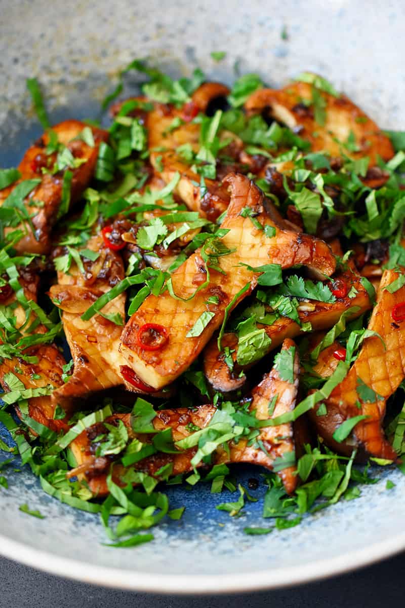 Close-up shot from the side of king oyster mushrooms with Thai Chili peppers, lime, and fresh herbs in a light blue bowl.